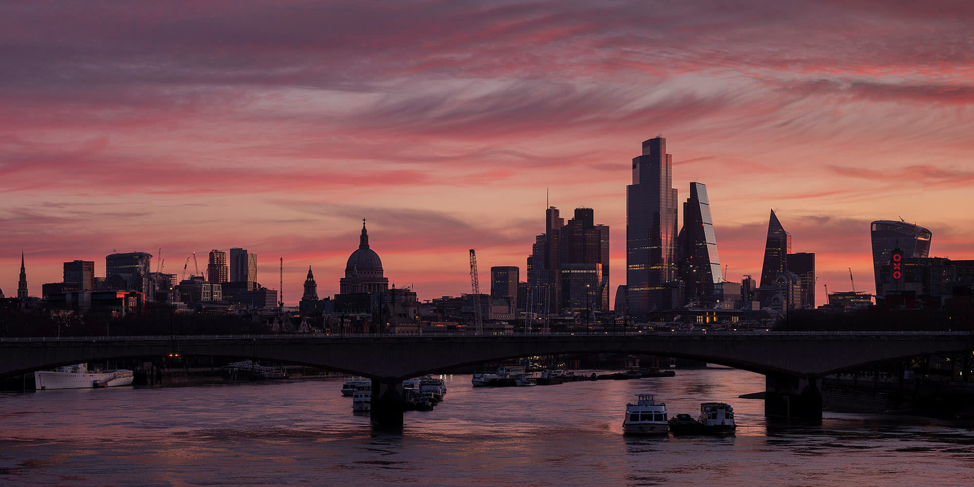 Photograph of London skyline under pink cloudy sky at dawn