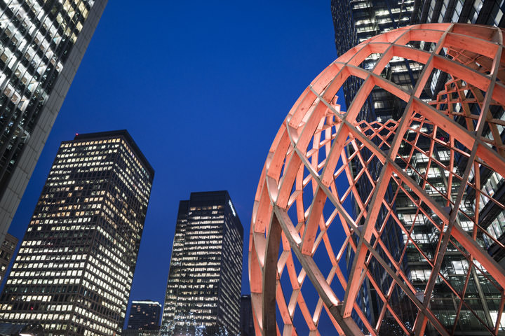 A red lit structure at Canary Wharf at dusk with a blue sky