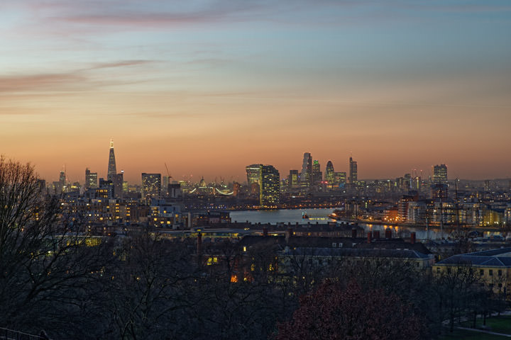 City of London skyline viewed from Greenwich under an orange sky.