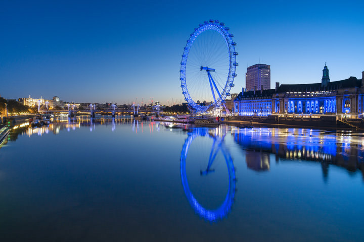 London Eye lit in blue at dawn with a deep blue sky and blue river thames