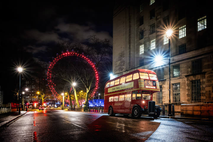 A Red Bus with the London Eye lit in red in the background at night