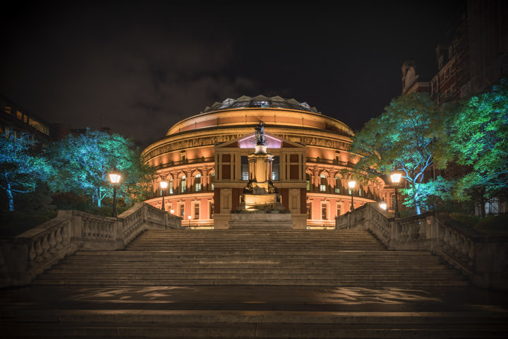 Royal Albert Hall at night brightly lit alongside green floodlit trees